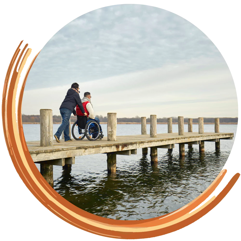 Disabled man in wheelchair being pushed along jetty by support worker